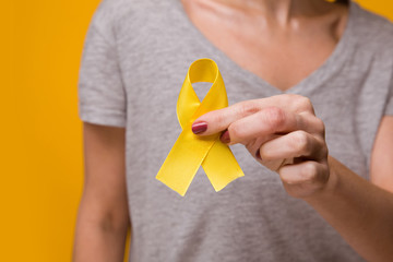 Woman with yellow ribbon on color background. Cancer awareness concept