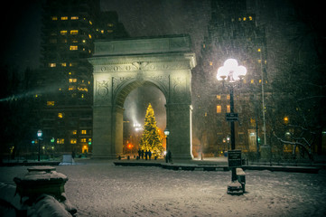 Winter holiday night view of the Washington Square Park with a Christmas Tree under falling snow in New York City