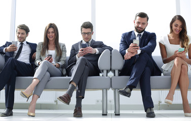 business colleagues with their smartphones sitting in the office hallway