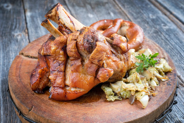 Traditionelle bayrische Schweinshaxe mit Krautsalat und Breze als closeup auf einem hölzernen Schneidebrett