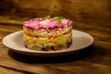 Traditional russian salad "Herring under a fur coat" (shuba) on wooden table. Layered salad with herring, beets, carrots, onions, potatoes and eggs