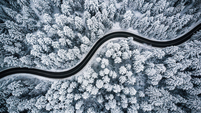 Curvy windy road in snow covered forest, top down aerial view