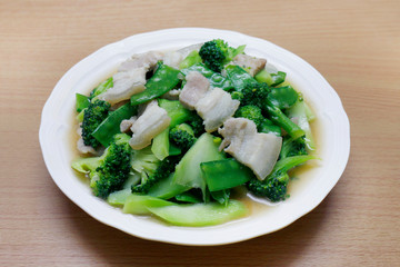 Stir Fried Broccoli, Peas with Crispy Pork with oyster sauce, Fried vegetable broccoli for food menu diet healthy in a dish on a wooden floor (Thai Foods)