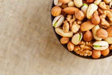 Mix of different nuts in a wooden cup against the background of fabric from burlap. Nuts as structure and background, macro. Top view.