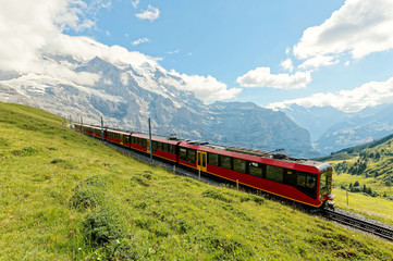 A cog wheel train travels on famous Jungfrau Railway from Kleine Scheidegg to Jungfraujoch station ( top of Europe ) on a green grassy hillside, in Berner Oberland ( Bernese Highlands ), Switzerland