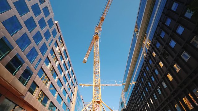 A large tower crane in the downtown of the modern city. Glass office buildings around. Low angle wide shot