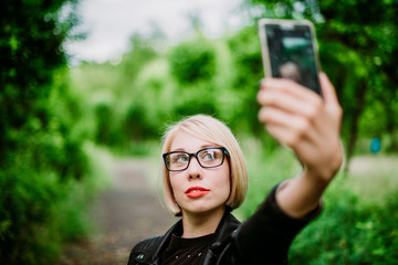 Girl in glasses makes selfie on a smartphone in a green park