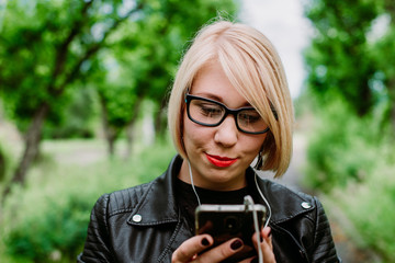 Nice girl in glasses listens to music on a smartphone in a green park park