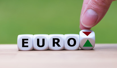 Hand is turning a dice and changes the direction of an arrow symbolizing that the value of the Euro...