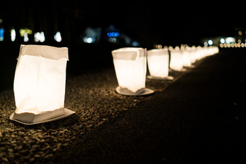 Christmas Eve candles illuminated in paper bags at night lights flame in row lining street road by residential neighborhood house decoration during holiday season on plates