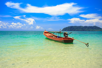 A fishing boat floating on beach with clean and clear sea and cloudy blue sky. Copy space.	