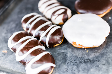 Chocolate brown and white icing long john eclair donuts closeup on bakery tray, deep fried vanilla, greasy tasty