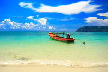 Fototapeta na wymiar A fishing boat floating on beach with clean and clear sea and cloudy blue sky. Copy space.