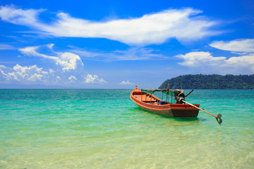 A fishing boat floating on beach with clean and clear sea and cloudy blue sky. Copy space.	