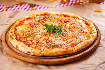 Italian Pizza with bacon, tomatoes and mozzarella cheese on wooden cutting board. Close up