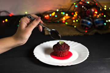 Red velvet cupcake with a woman’s arm and teaspoon, cupcake in a plate on the table in low key