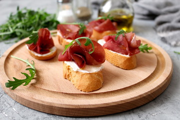 Canape or crostini with toasted baguette, light cheese, bresaola and arugula on wooden board. Diet food. Iron food.