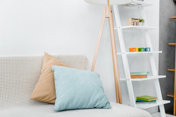 modern pillows on sofa near wooden lamp and toys on rack