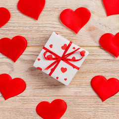 Valentine or other holiday handmade present in paper with red hearts and gifts box in holiday wrapper. Present box of gift on orange wooden table top view with copy space, empty space for design