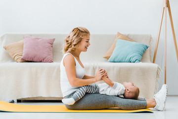  woman sitting on fitness mat and playing with toddler son