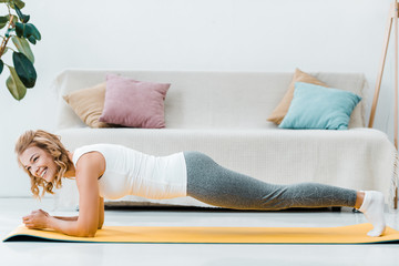 smiling woman in sportswear doing plank on yellow fitness mat at home