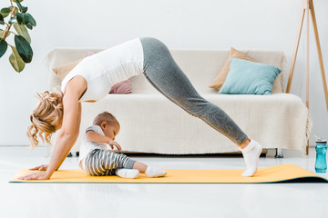 woman doing exercise and toddler boy lying on fitness mat at home