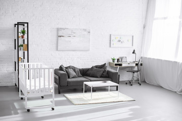 modern interior of living room with baby crib, sofa and workplace