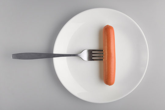 Concept diet, healthy food. One sausage on a white plate, sausage on a fork on a gray background.