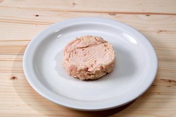Solid white albacore tuna fish up close on white plate still shaped like the can it came in on wooden table.