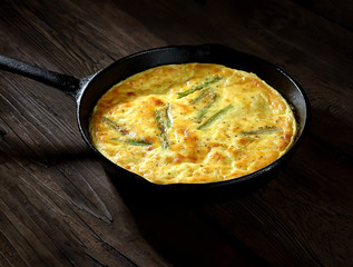 omelet with asparagus in a pan on a wooden background. rustic style.