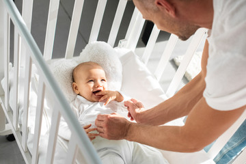 cropped view of father putting infant daughter into baby crib - Powered by Adobe