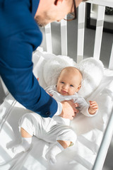 cropped view of father in suit putting infant daughter into baby crib