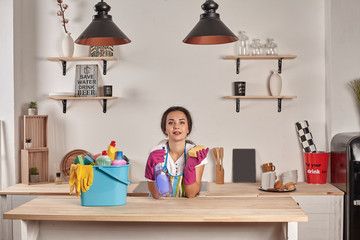 Woman wearing gloves, holding with a sponge in his hands, bowl full of bottles with disinfectant on table