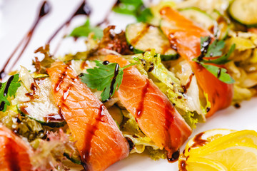 Salad with salmon, cucumber and mixed greens on white plate. Close up