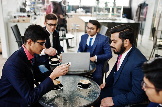 Group of five indian business man in suits sitting at office on cafe looking at laptop and drinking coffee.
