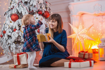 Child with mom with gifts near the Christmas tree. Mother and little daughter together with present indoors. New Year's and Xmas holidays