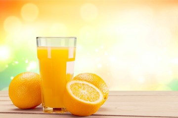 Glass of fresh orange juice on blurred light background