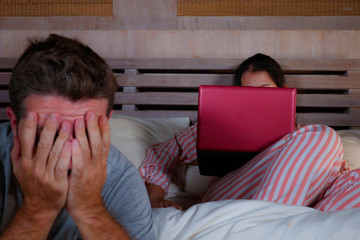 angry and frustrated husband moody in bed ignored by his workaholic wife or internet social media addict girlfriend using laptop in bed ignoring the man in couple problem