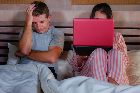 Angry And Frustrated Husband Moody In Bed Ignored By His Workaholic Wife Or Internet Social Media Addict Girlfriend Using Laptop In Bed Ignoring The Man In Couple Problem