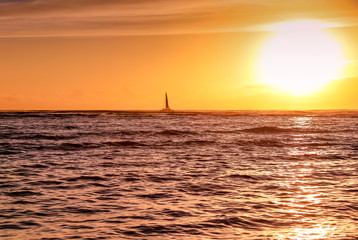 silhouette of sail boat with bright orange sun at sunset