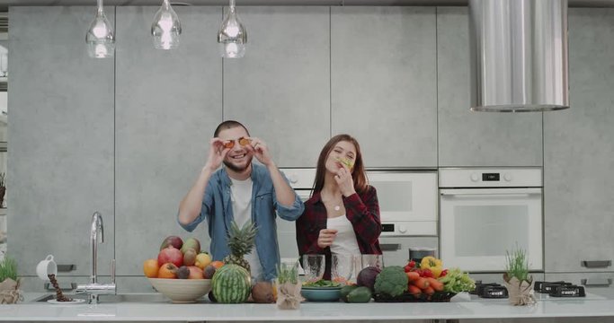 In a modern kitchen a young couple spending a funny time together making mustaches from vegetables before making the healthy breakfast.