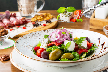Greek salad with feta cheese, olives and herbs, served in a white plate on a table in a restaurant.