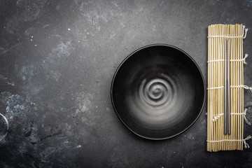 Obraz premium Empty plate (dark) and Chinese chopsticks on a dark background. Asian style, Asian cuisine. Copy space.