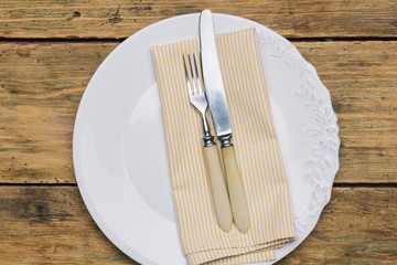 Empty white rustic plate on old wooden background with knife, fork and napkin. Rustic food concept. Copy space