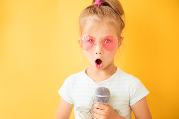 Happy little girl singing into a microphone the song on yellow background