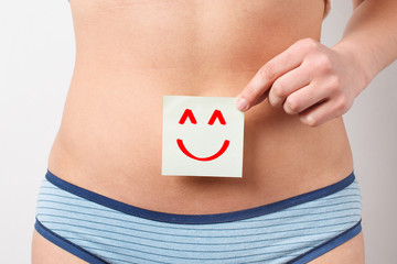 Women Health. Closeup Of Healthy Female With Beautiful Fit Slim Body Holding White Card With Happy Smiley Face. Stomach Health And Good Digestion Concepts