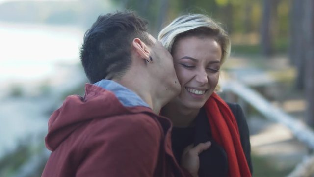 Young couple on a date outdoors. Asian guy kisses his caucasian girlfriend. Beautiful interracial couple in casual wear is relaxing in nature and spending time together.