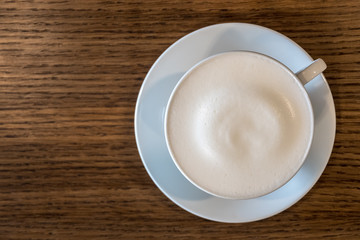 A cup of coffee with milk froth on wooden table background with copy space