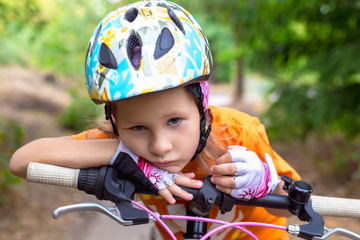 Obraz premium Cute little sad girl in a helmet with a bike in the summer