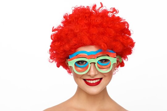 Portrait of a young woman in the image of a clown with a red wig on her head